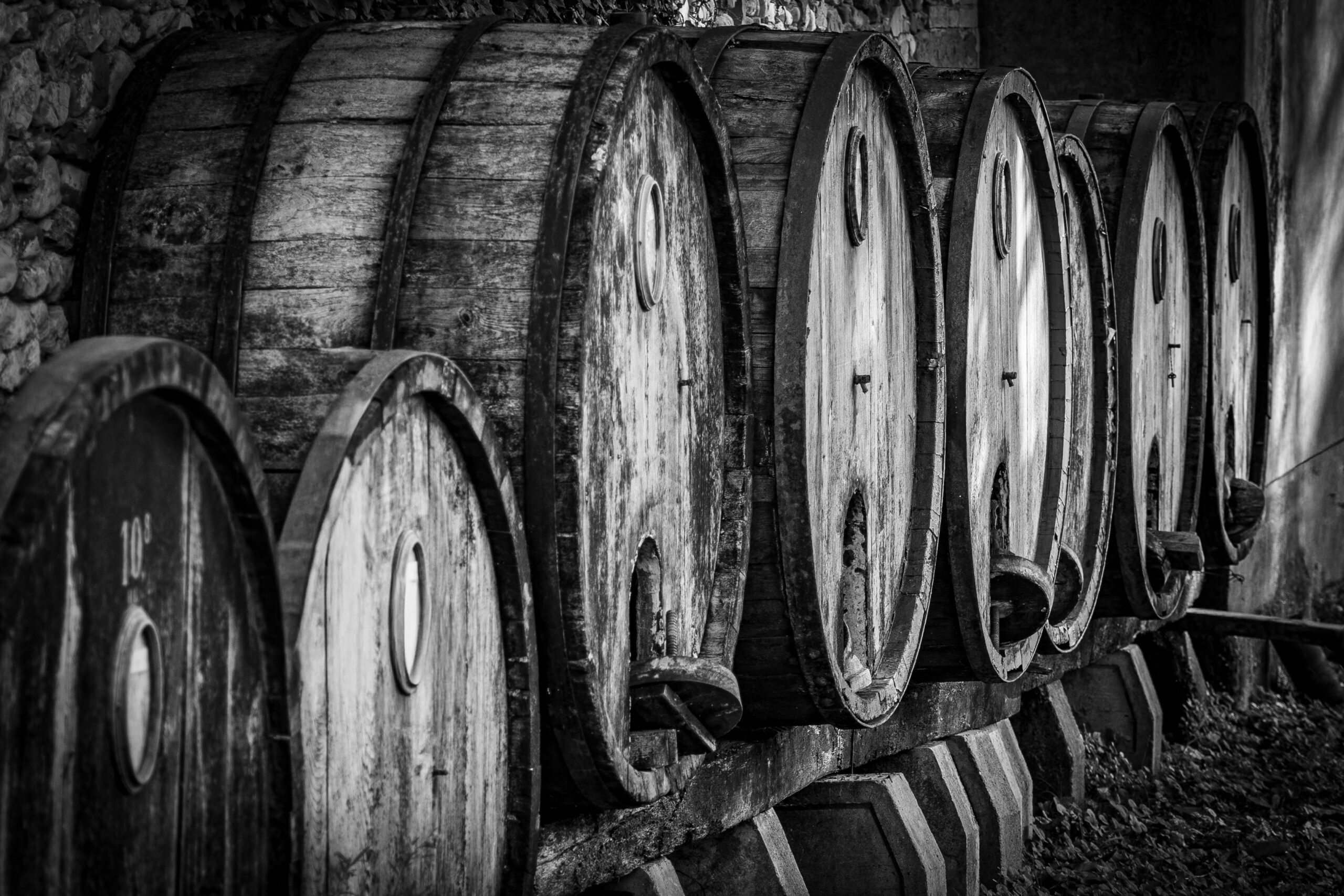 A row of vintage wooden wine barrels in a cellar, showcasing rustic textures in monochrome.
